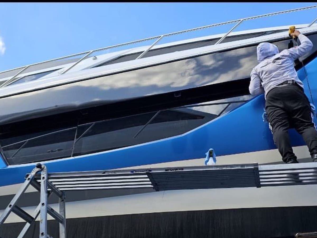 Installer working along the windows of a blue hull